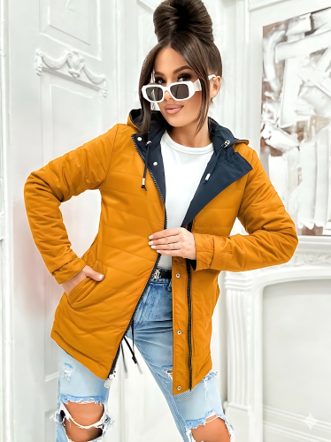 obieta w musztardowej kurtce wiosennej o kroju parki. Widoczne kontrastowe granatowe wykończenie przy mankietach i zamku.