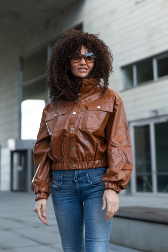 Brązowa kurtka damska z eko-skóry o kroju oversize. Model wiosenny zapinany na guziki, z szerokimi rękawami i elastycznym ściągaczem na dole.